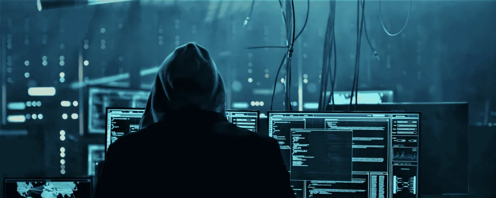 Hooded person looking at lots of computer monitors