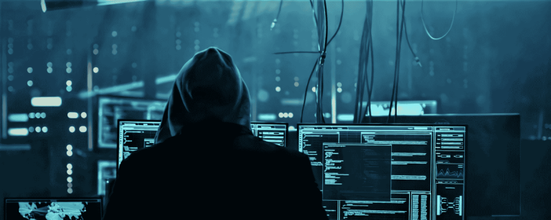Hooded person looking at lots of computer monitors